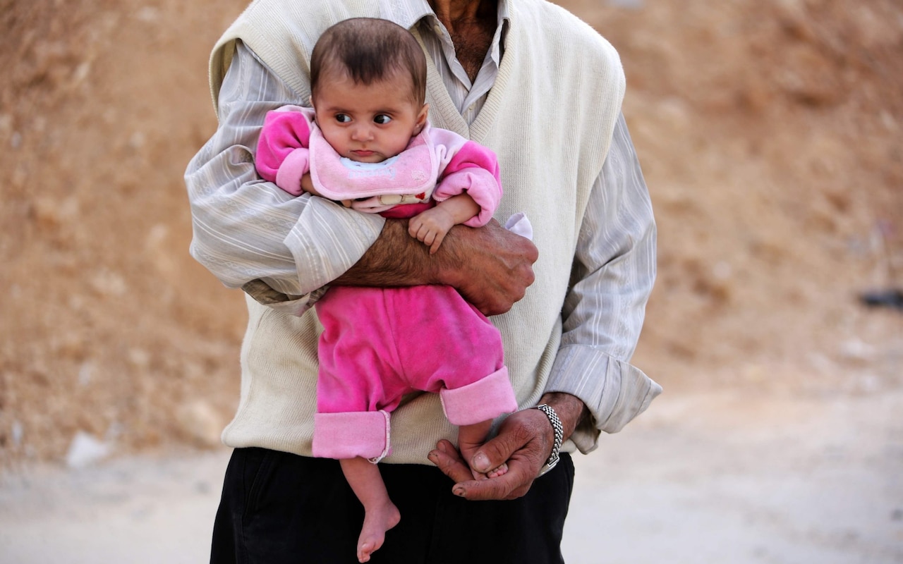 A man walks down a destroyed street carrying an infant in the former rebel-held Syrian town of Douma