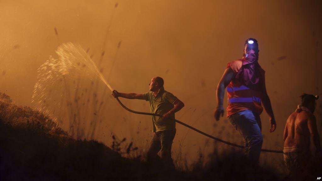 Volunteers use a water hose to fight a wild fire raging near houses in the outskirts