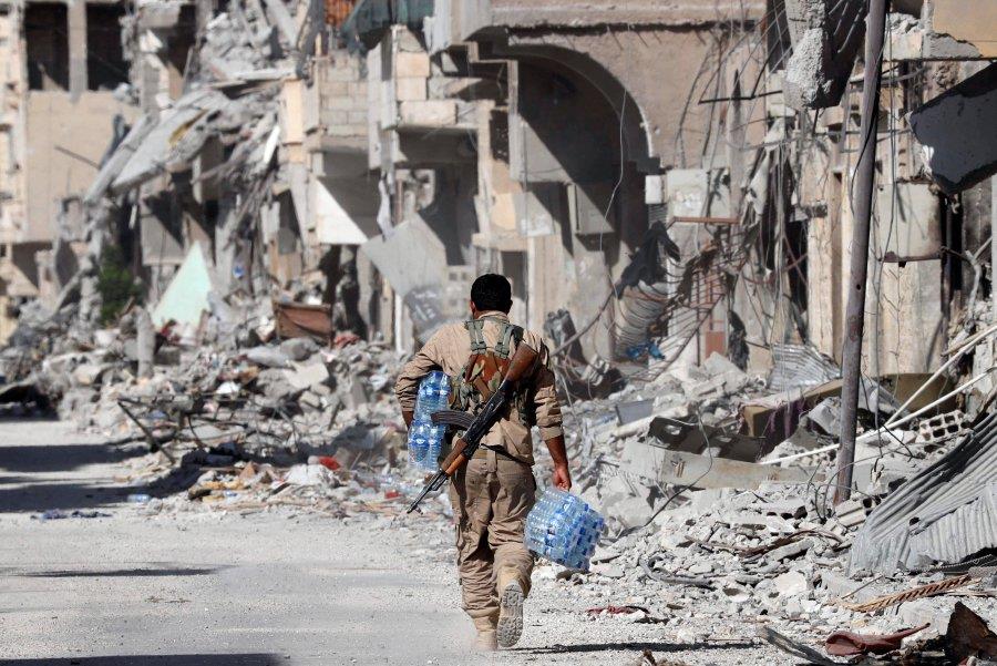 A member of Syrian Democratic Forces carries bottles of mineral water for his comrades along a street in the Old City of Raqqa, Syria October 1, 2017.