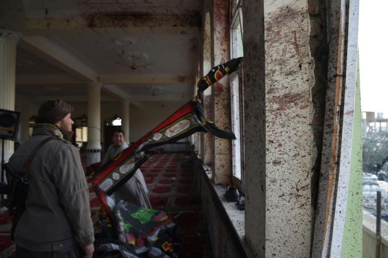 An armed Afghan civilian and a resident collect religious flags as they look the Imam Zaman Shiite mosque which was a the site of a suicide attack during evening prayers, in Kabul on October 21, 2017