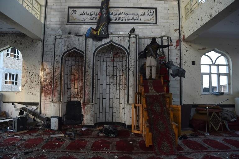 An armed Afghan civilian and a resident collect religious flags as they look the Imam Zaman Shiite mosque which was a the site of a suicide attack during evening prayers, in Kabul on October 21, 2017