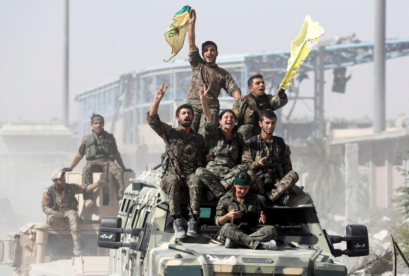 Syrian Democratic Forces (SDF) fighters ride atop military vehicles as they celebrate victory in Raqqa, Syria, October 17, 2017