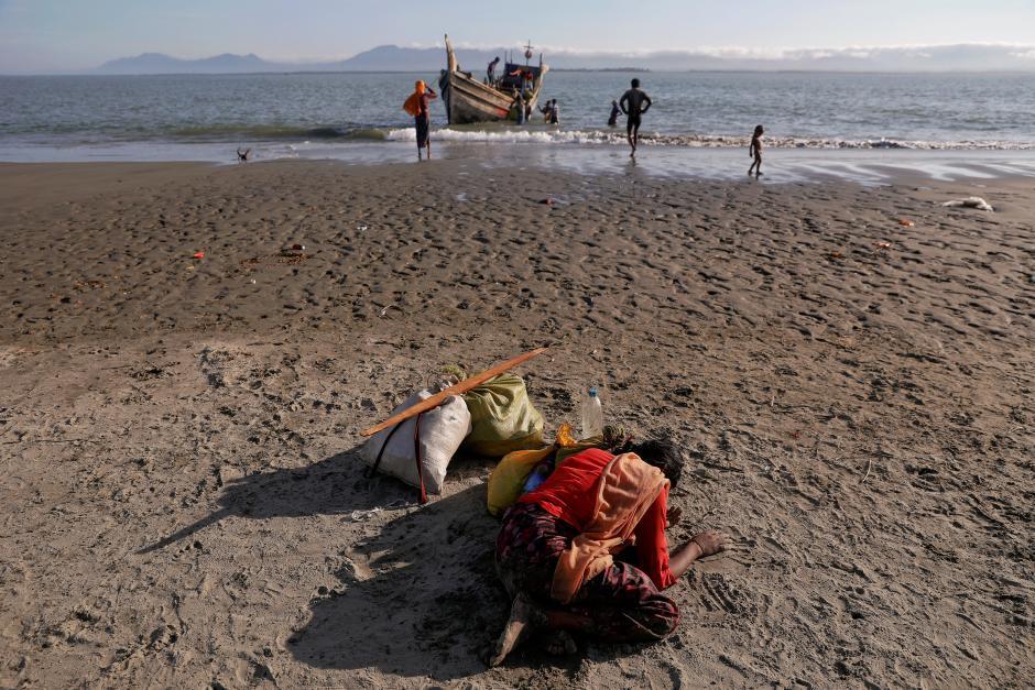 Shakira, a 22 year old, collapses from exhaustion as Rohingya refugees arrive by a wooden boat from Myanmar to the shore of Shah Porir Dwip