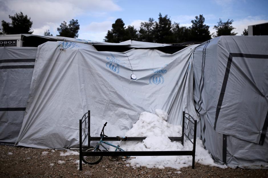 Snow is gathered under a broken bicycle and a bed frame next to a tent at a refugee camp in Ritsona, northern of Athens, Greece