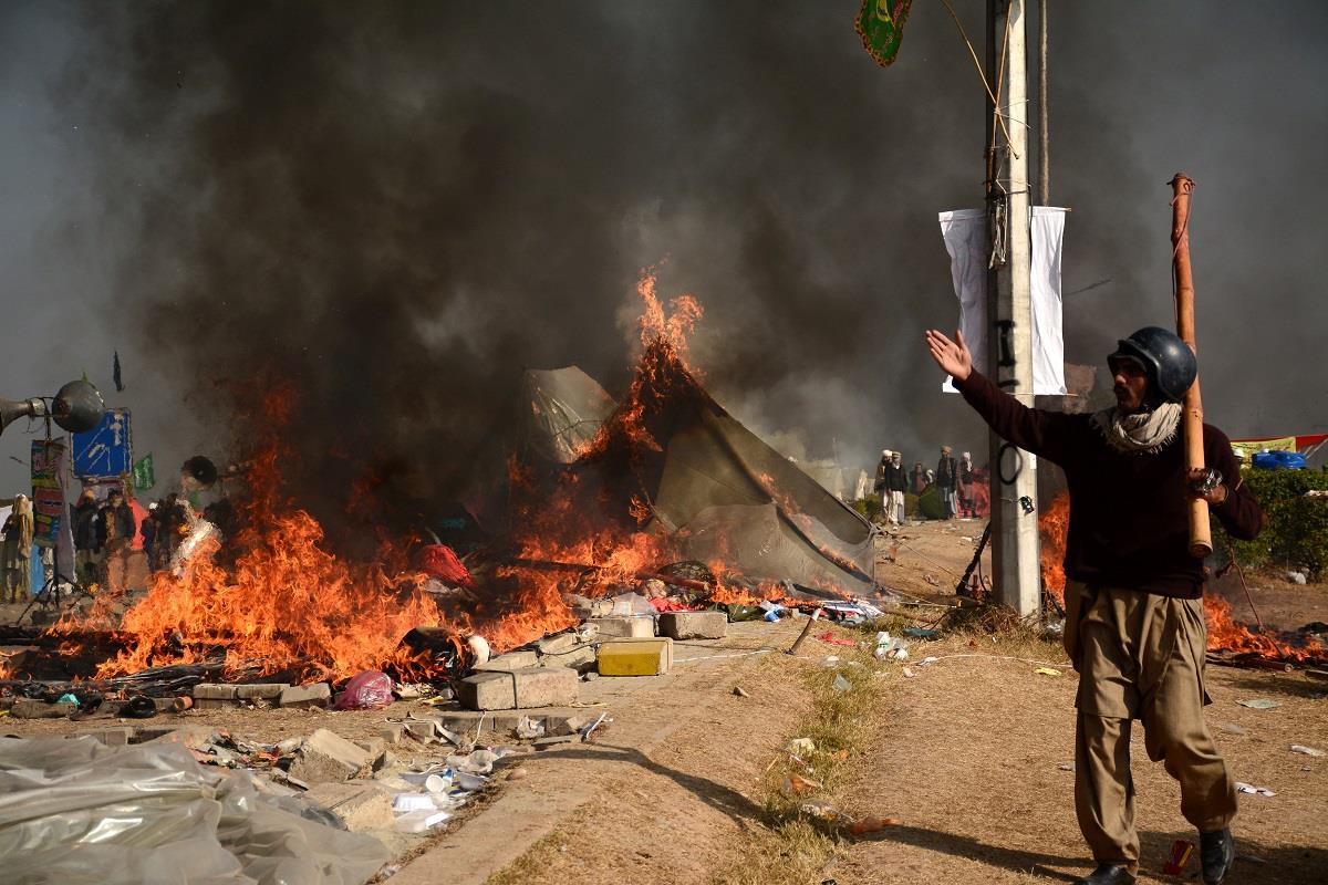 A protester walks near burning tents during clashes with police at Faizabad junction in Islamabad. 
