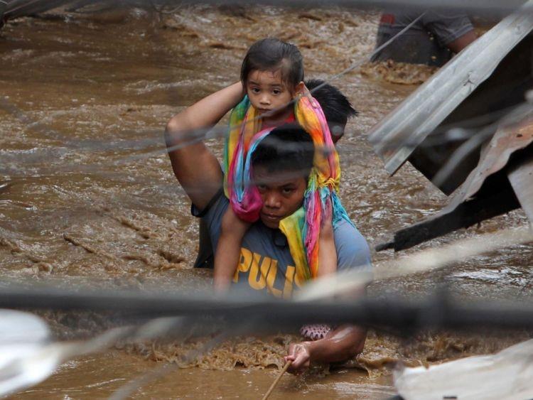 Image: A policeman carries a young girl along a flooded street in Cagayan City
