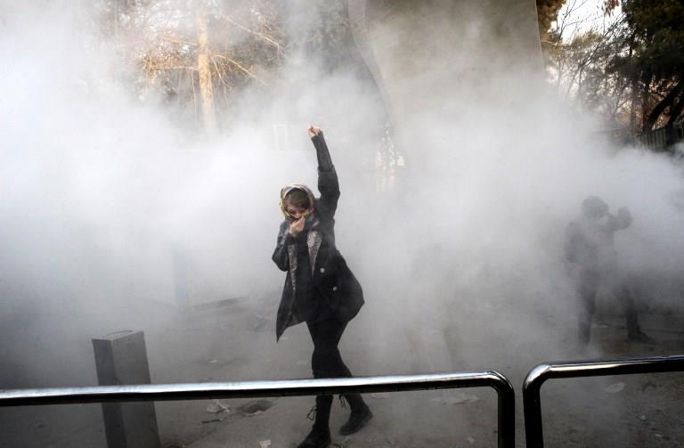 An Iranian woman raises her fist amid the smoke of tear gas at the University of Tehran during a protest driven by anger over economic problems