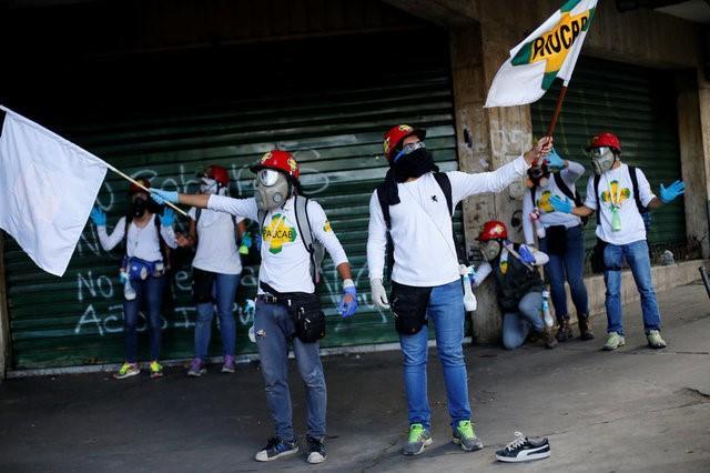 Volunteers members of a primary care response team raise their hands as riot security forces ride close by during a rally against Venezuela's President