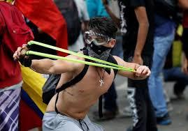 A demonstrator uses a sling shot while clashing with riot security during a rally against Venezuela's President Nicolas Maduro's government in Caracas