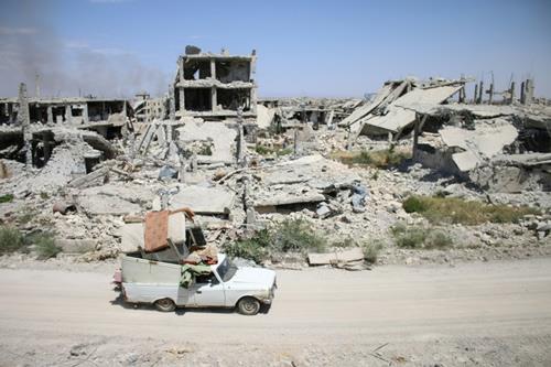 A car loaded with belongings of a displaced Syrian family drives past destroyed buildings in a rebel-held area of the southern city of Daraa in May 2017