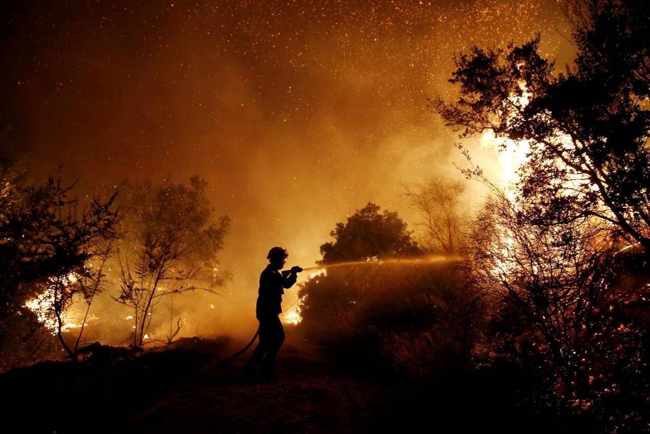 Firefighters battle spreading wildfire near Athens, homes damaged. A firefighter tries to extinguish a wildfire burning near the village of Kalamos