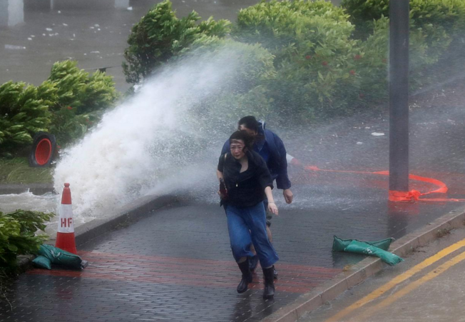 People react as Typhoon Hato hits Hong Kong, people are passing through a street in the wind and severe storms