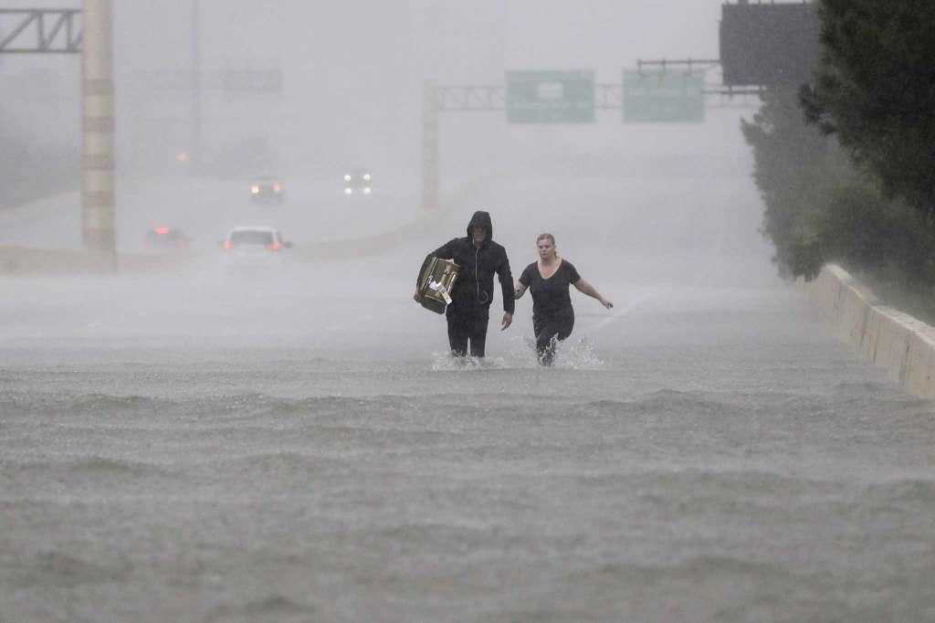 Two people walk down a flooded section of Interstate 610 in floodwaters from Tropical Storm Harvey