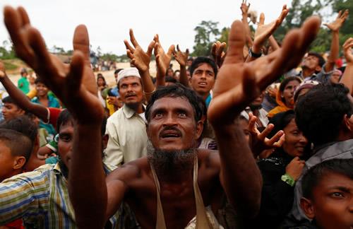 Rohingya refugees stretch their hands to receive food distributed by local organizations in Kutupalong