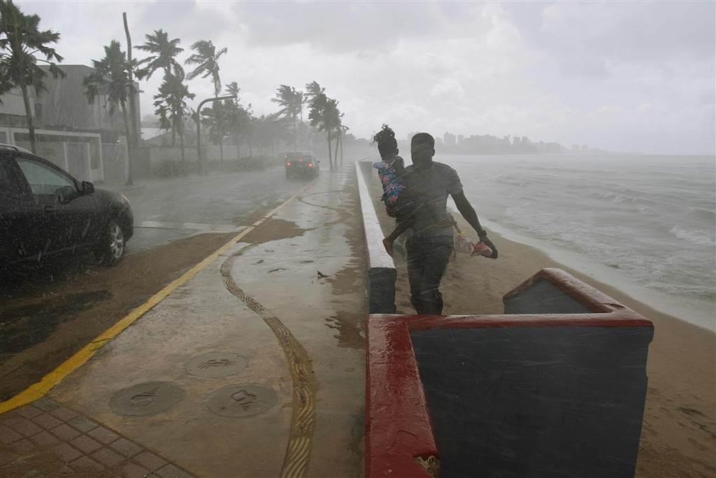 A man and his daughter make their way through rain on a beach in San Juan on Sept. 19, prior to the arrival of Hurricane Maria.