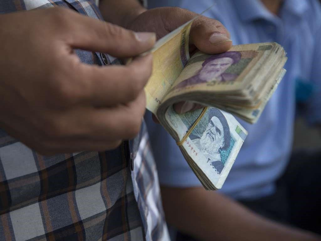 street trader counts out rial banknotes in Tehran, Iran. 