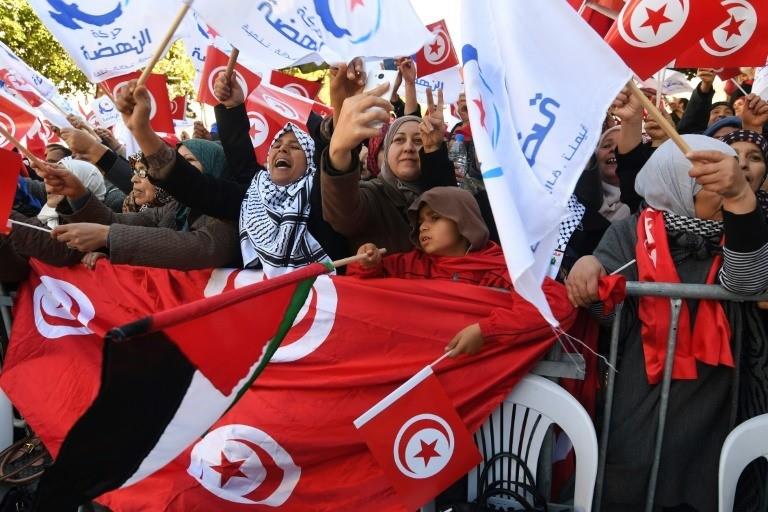 Tunisians wave their national flag and the flag of the Ennahda Islamist party as they gather on Habib Bourguiba Avenue in Tunis on January 14, 2018