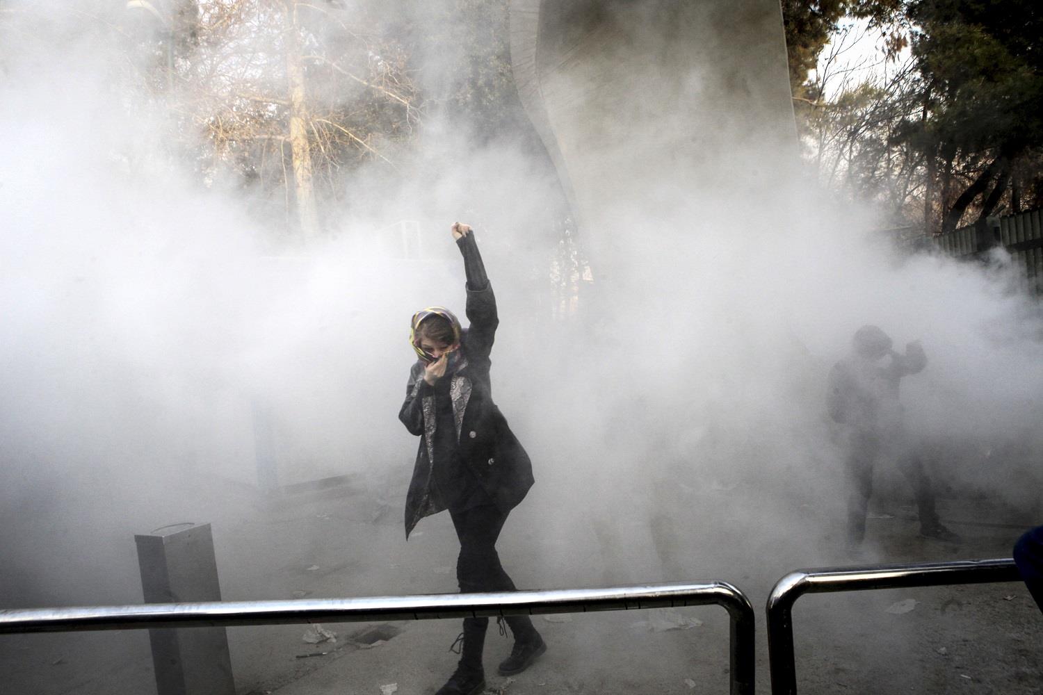 A university student attends a protest inside Tehran University while a smoke grenade is thrown by anti-riot Iranian police, in Tehran, Iran, Saturday, Dec. 30, 2017. (AP)